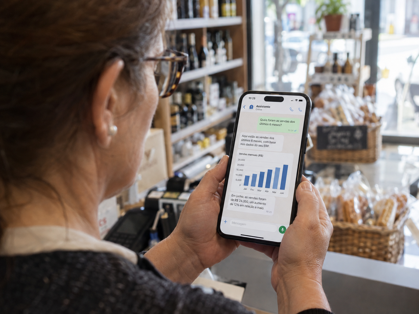 Dona de loja atrás do balcão a perguntar as vendas ao ERP em linguagem natural, num chat estilo WhatsApp no telemóvel